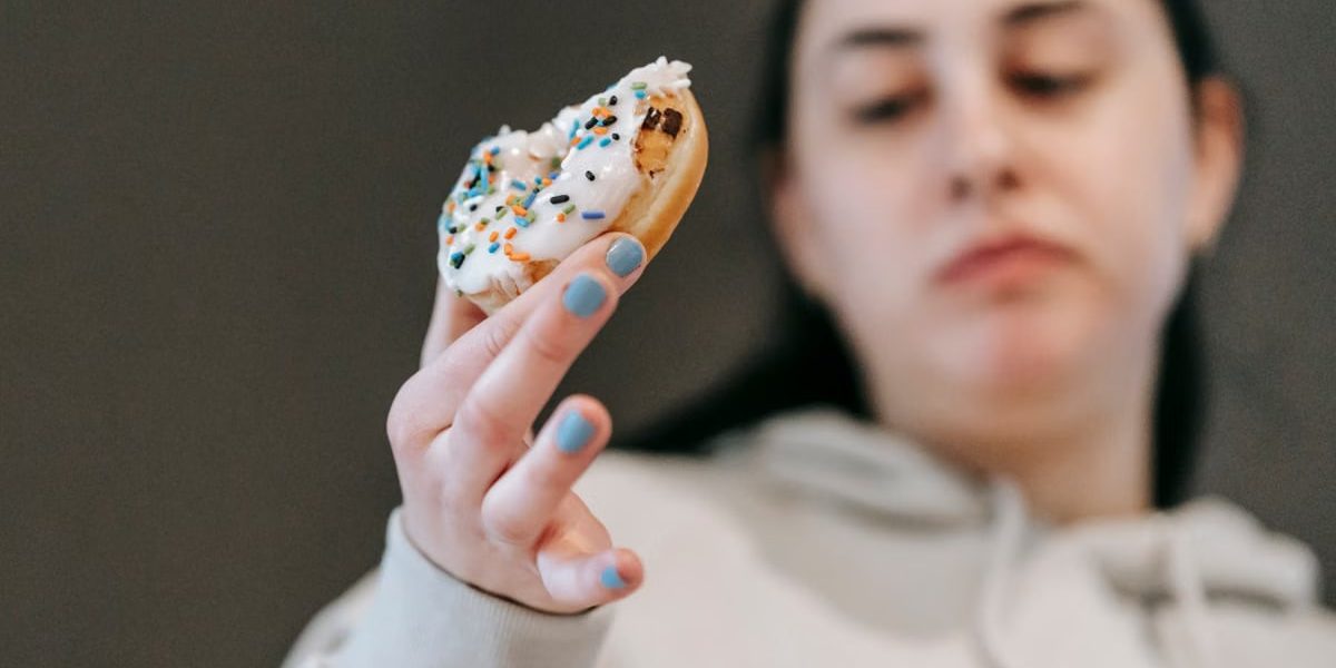Crop emotionless female in casual wear chewing tasty doughnut glazed with vanilla icing in light room