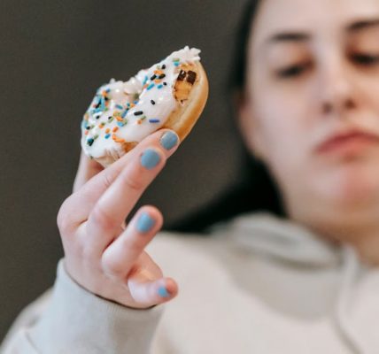 Crop emotionless female in casual wear chewing tasty doughnut glazed with vanilla icing in light room